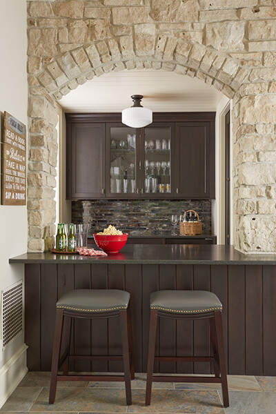 Cozy home bar with dark cabinetry and a stone archway, designed by MA Peterson in Twin Cities