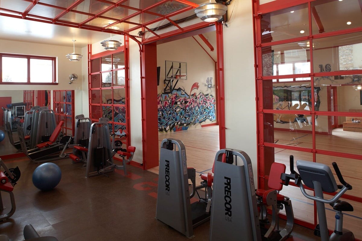 Fitness room with red accents and a view of an indoor basketball court, designed by MA Peterson in the Twin Cities