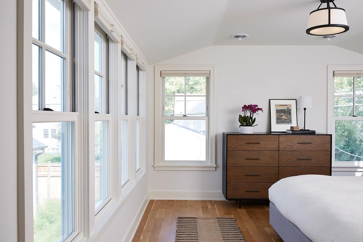 Bright bedroom with large windows and a wooden dresser, part of a custom home by MA Peterson in the Twin Cities