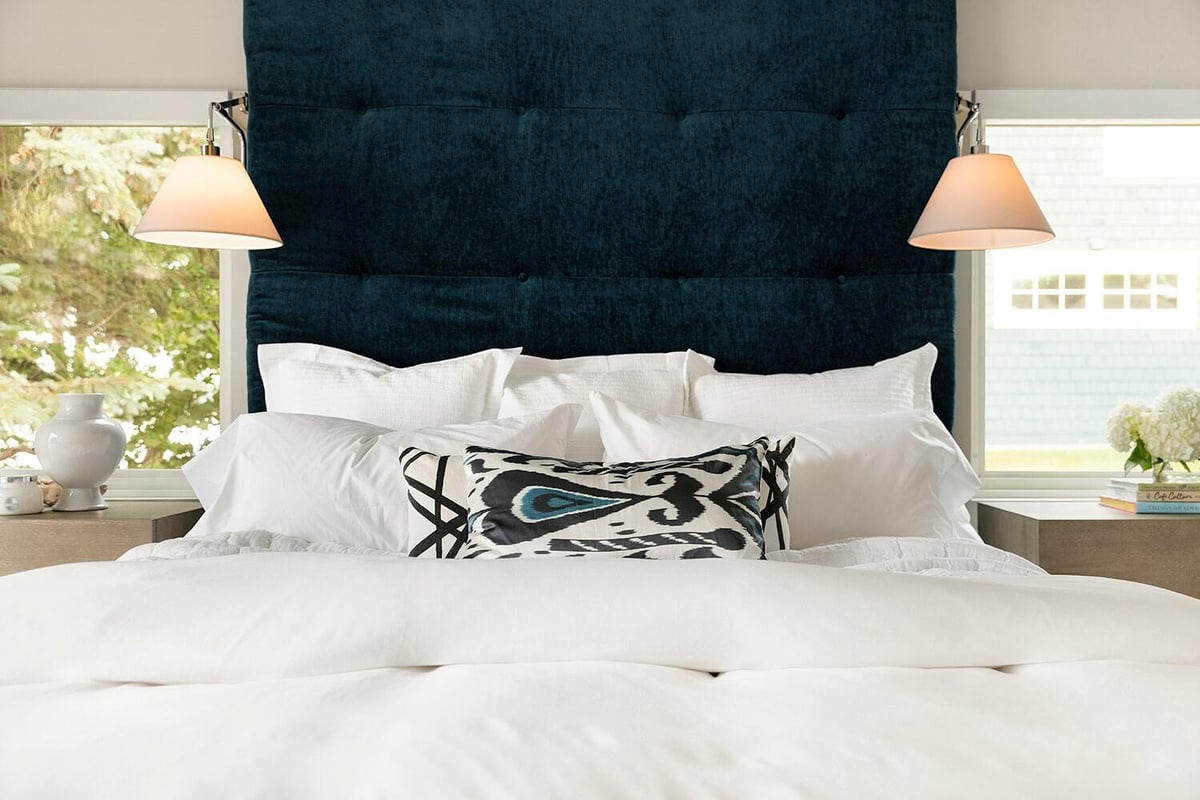 Close-up of a plush bed with a blue headboard and stylish pillows in a custom home by MA Peterson in the Twin Cities