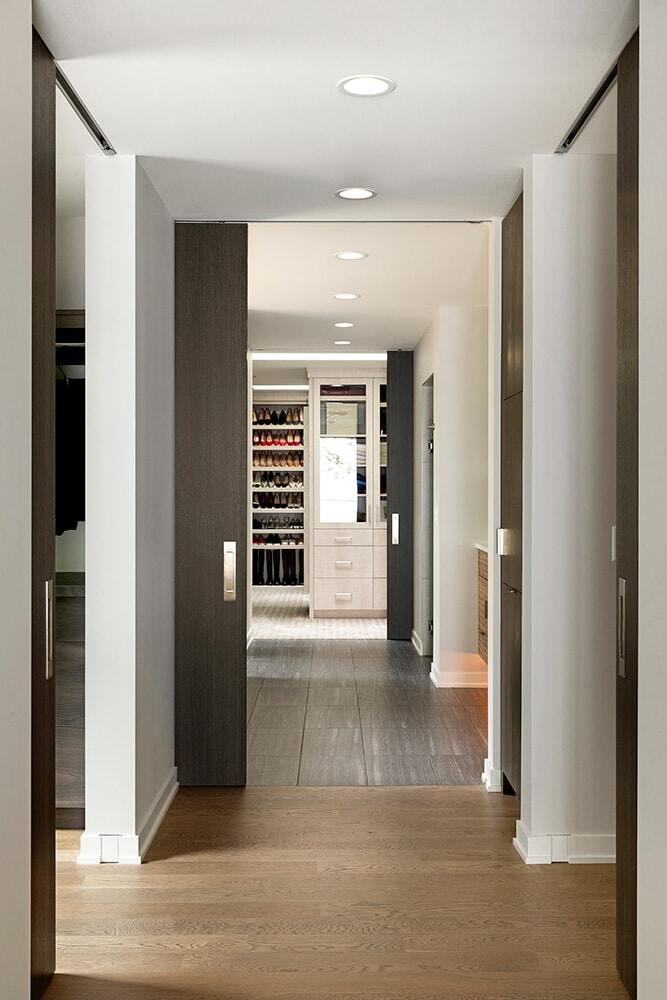 Hallway leading to a walk-in closet with organized shelves and shoe racks in a custom home by MA Peterson in the Twin Cities