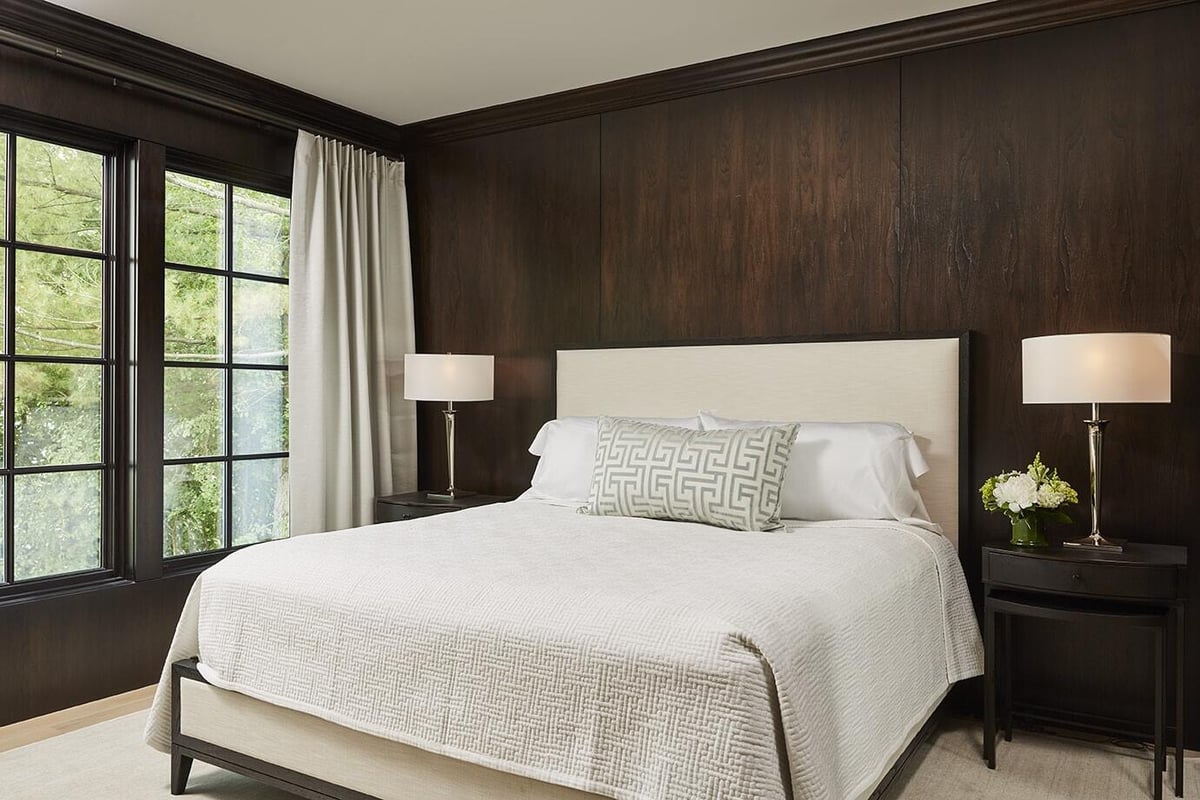 Modern bedroom with dark wood paneling and large windows, showcasing a comfortable bed by MA Peterson, Twin Cities