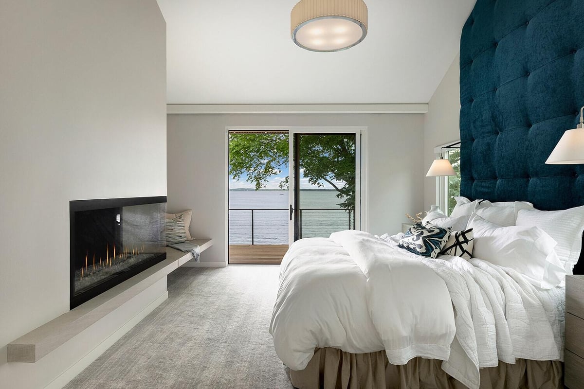 Stylish bedroom with a scenic lake view, featuring a modern fireplace and a blue tufted headboard, custom home by MA Peterson, Twin Cities