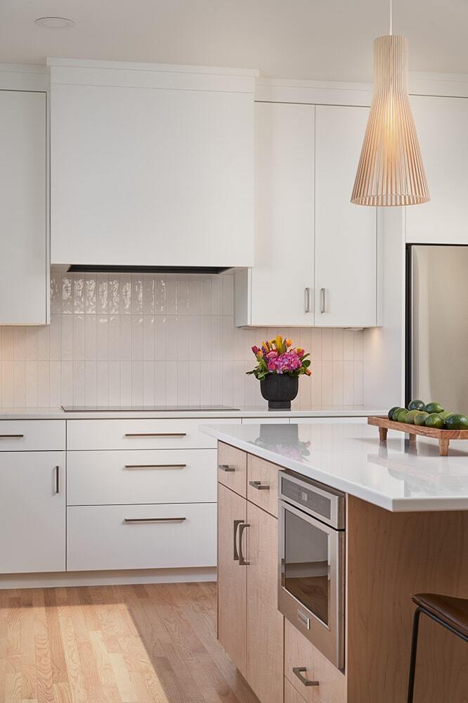 White kitchen with island and pendant light in Crafting Warmth in Modern home by MA Peterson, Twin Cities