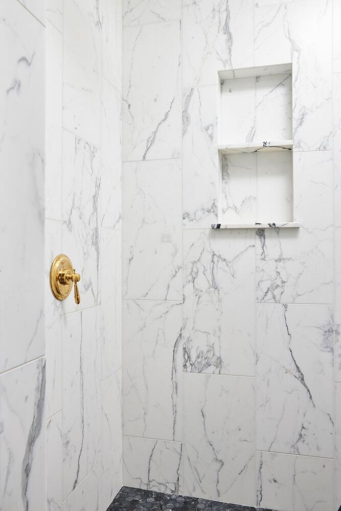 White marble shower with built-in shelves and gold shower fixtures by MA Peterson in Twin Cities